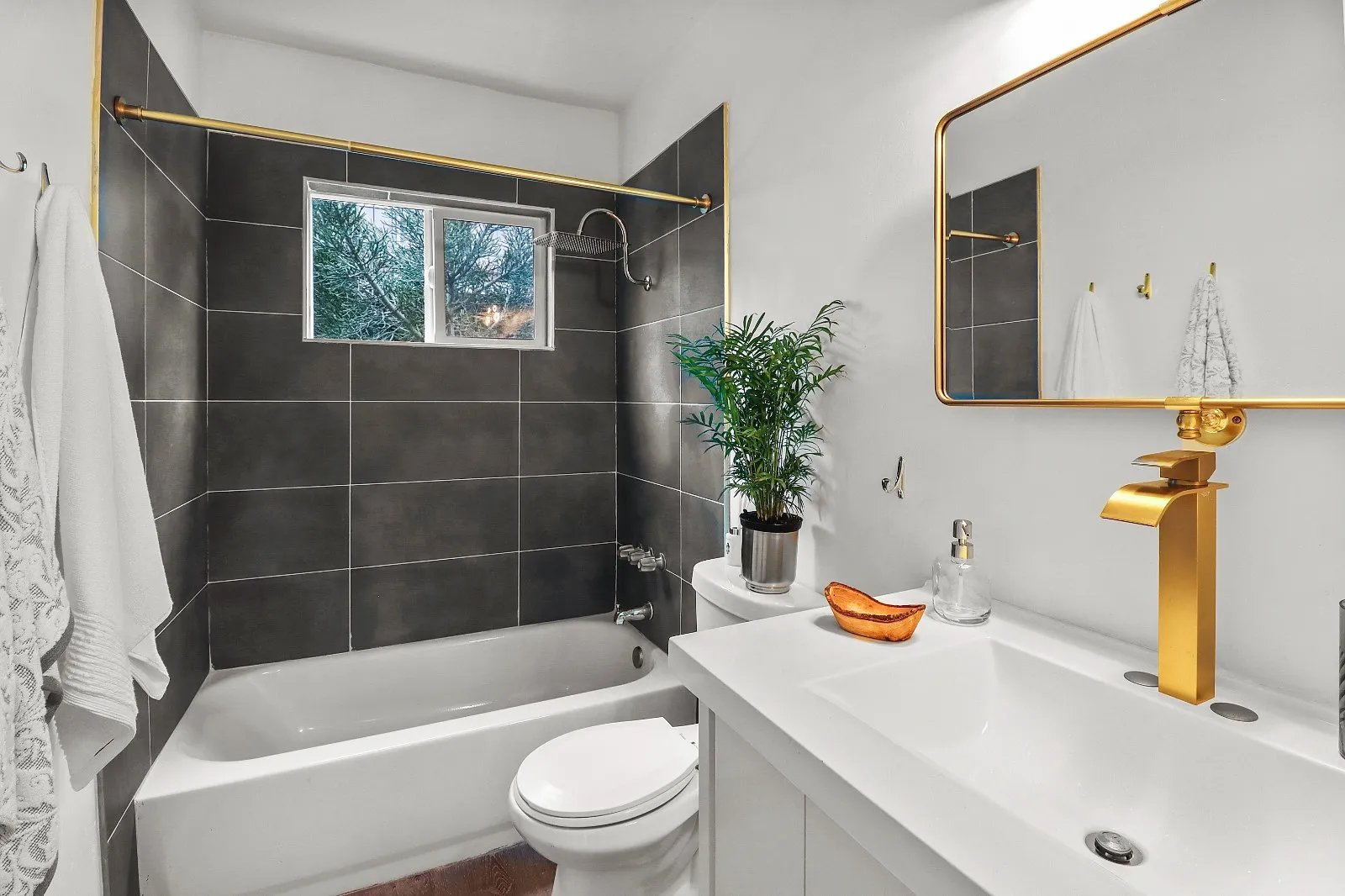 Renovated bathroom with large-format charcoal wall tile, a brass basin tap and a framed mirror