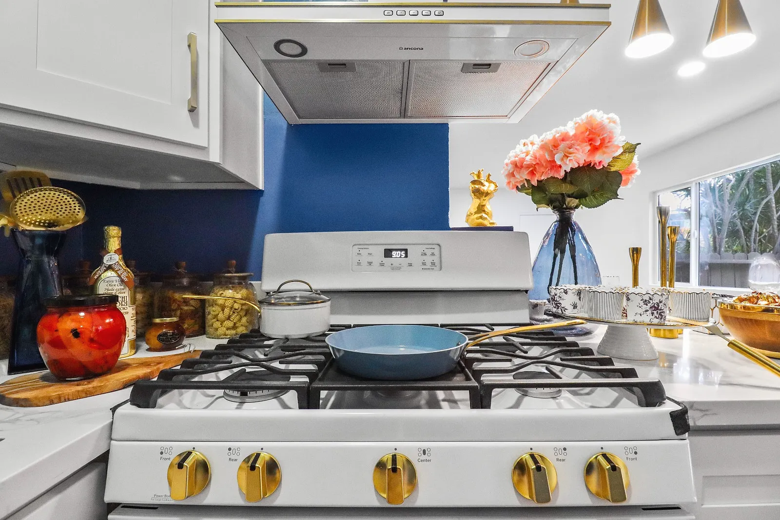 Close view of a finished kitchen range with brass control knobs, a stainless hood and a blue tiled wall